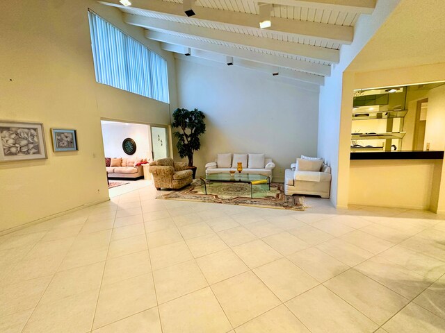 living room featuring a wealth of natural light, light tile patterned floors, beamed ceiling, and a high ceiling