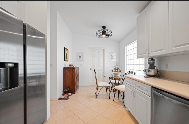 kitchen with vaulted ceiling, appliances with stainless steel finishes, light tile patterned floors, and white cabinets