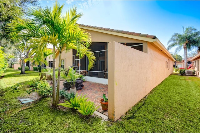 view of side of property with central AC unit, a yard, a sunroom, and a patio