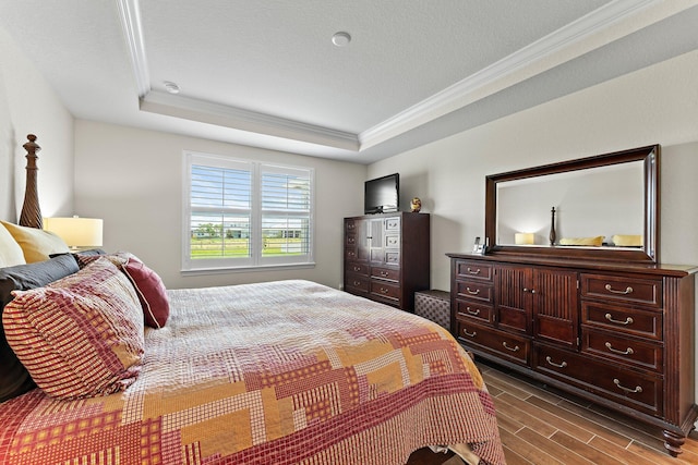 bedroom with hardwood / wood-style floors, crown molding, and a raised ceiling