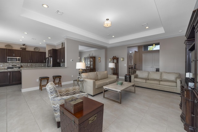 living room with light tile patterned flooring, a tray ceiling, and crown molding