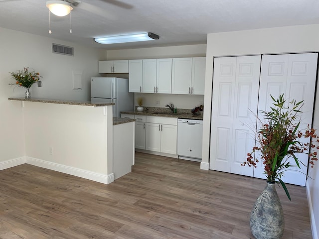 kitchen with dark stone countertops, sink, white appliances, hardwood / wood-style flooring, and white cabinets