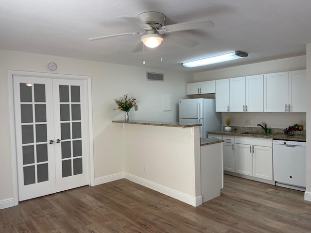 kitchen featuring white appliances, white cabinets, dark hardwood / wood-style flooring, dark stone counters, and sink