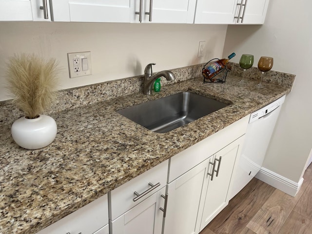 kitchen with dark stone countertops, sink, white dishwasher, white cabinets, and dark hardwood / wood-style flooring