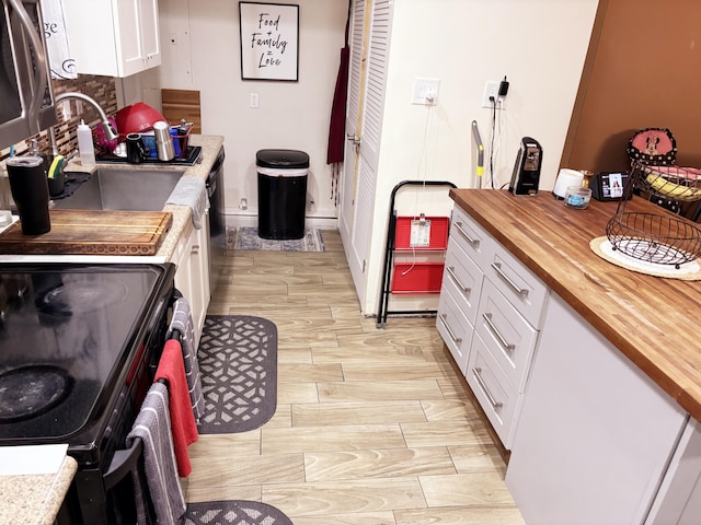 kitchen with white cabinetry, wooden counters, black electric range oven, and sink