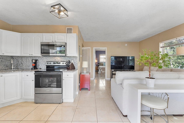 kitchen with stainless steel appliances, light tile patterned floors, decorative backsplash, white cabinets, and sink