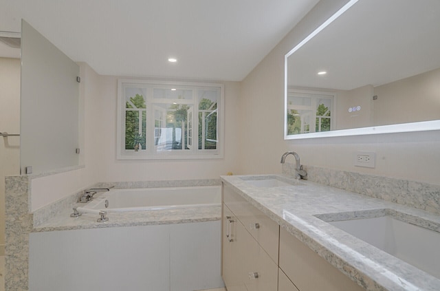 bathroom featuring tiled bath, a wealth of natural light, and vanity