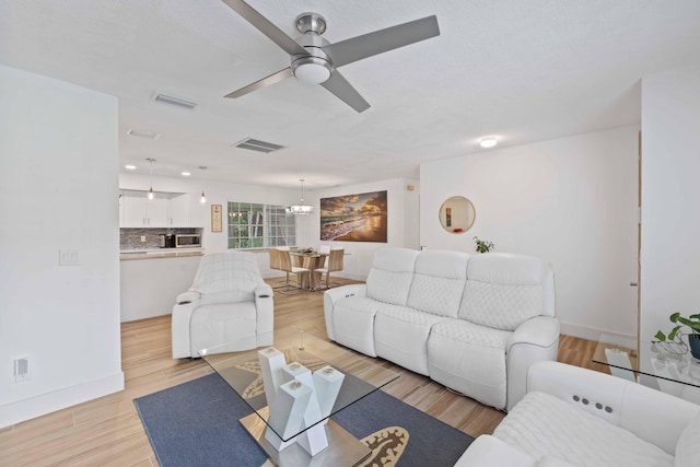 living room featuring ceiling fan with notable chandelier and light wood-type flooring