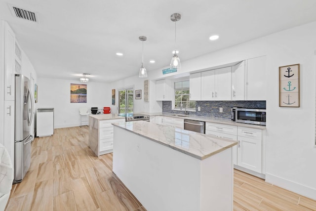 kitchen with white cabinets, appliances with stainless steel finishes, a center island, hanging light fixtures, and kitchen peninsula