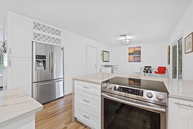 kitchen with light stone countertops, appliances with stainless steel finishes, white cabinetry, and light hardwood / wood-style flooring