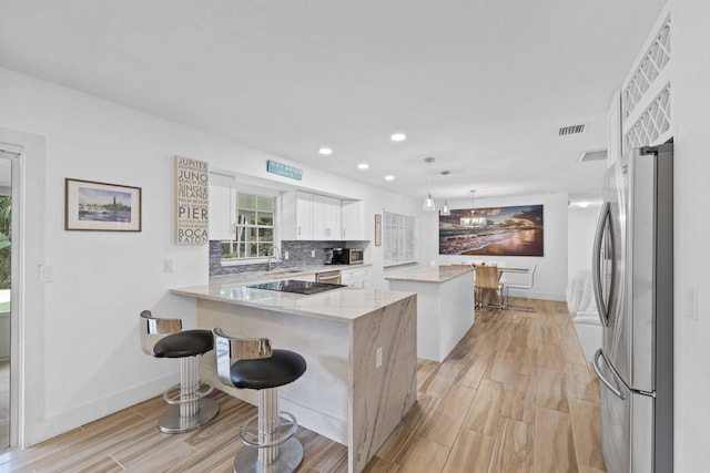 kitchen with white cabinetry, kitchen peninsula, appliances with stainless steel finishes, decorative light fixtures, and a kitchen island