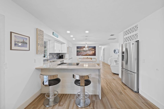 kitchen with stainless steel fridge with ice dispenser, kitchen peninsula, backsplash, white cabinets, and a breakfast bar