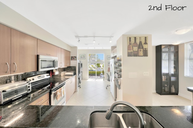 kitchen with sink, dark stone countertops, stainless steel appliances, and light tile patterned flooring