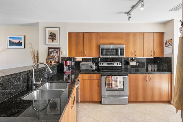 kitchen with tasteful backsplash, dark stone countertops, sink, appliances with stainless steel finishes, and light tile patterned floors