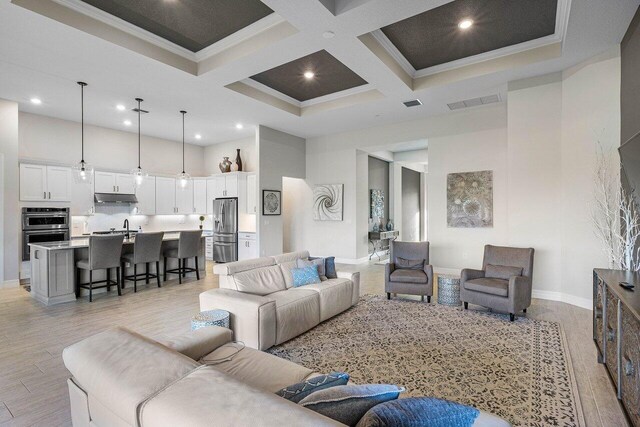 living room featuring a high ceiling, crown molding, light hardwood / wood-style floors, beam ceiling, and coffered ceiling