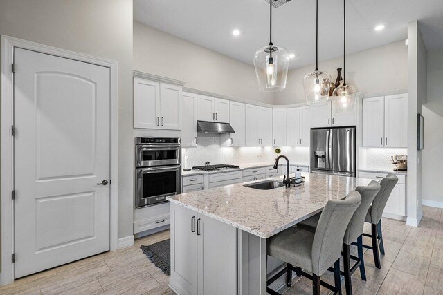 kitchen featuring sink, white cabinets, stainless steel appliances, and a kitchen island with sink