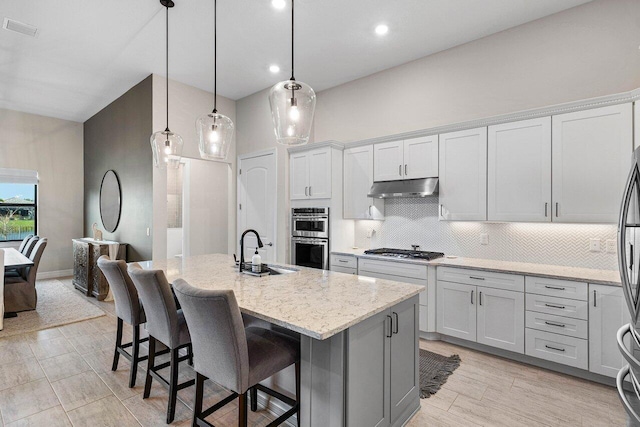 kitchen with decorative light fixtures, sink, a kitchen island with sink, appliances with stainless steel finishes, and a breakfast bar area