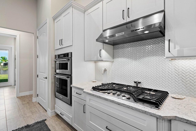 kitchen with appliances with stainless steel finishes, backsplash, white cabinets, and light stone countertops