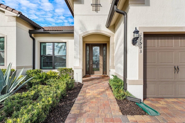 view of exterior entry with a tiled roof, an attached garage, and stucco siding