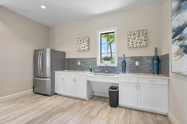 kitchen with backsplash, sink, stainless steel refrigerator, light wood-type flooring, and white cabinets