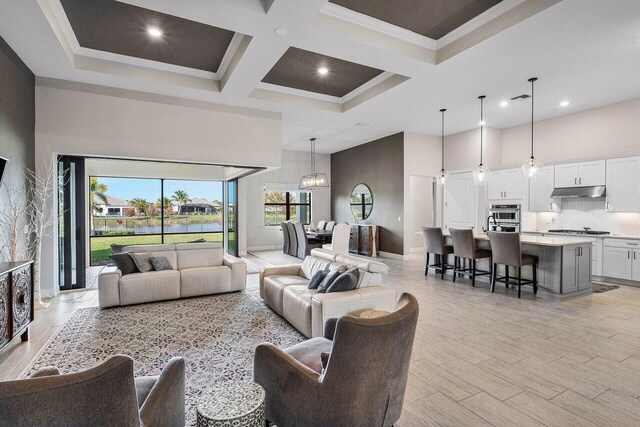 living room with coffered ceiling, a wealth of natural light, a high ceiling, and ornamental molding