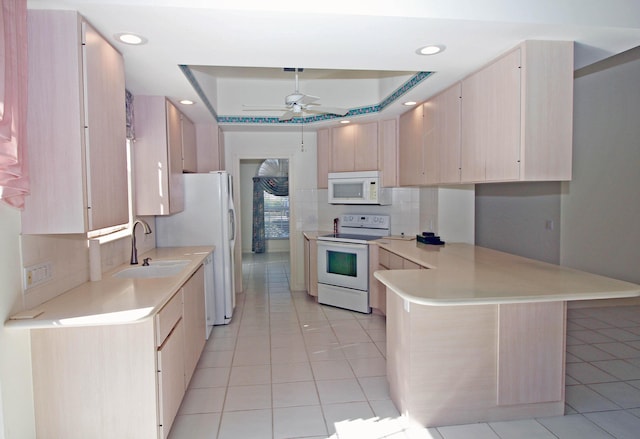 kitchen with ceiling fan, kitchen peninsula, sink, a tray ceiling, and white appliances