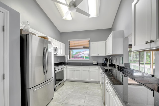 kitchen featuring vaulted ceiling, dark stone countertops, sink, appliances with stainless steel finishes, and white cabinets