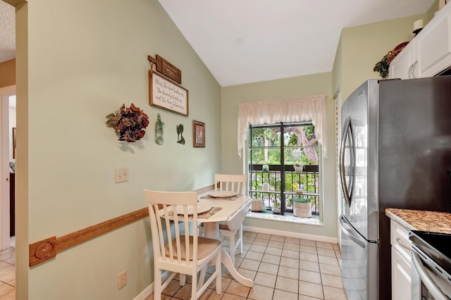 kitchen featuring light tile patterned flooring, white cabinetry, vaulted ceiling, and stainless steel fridge