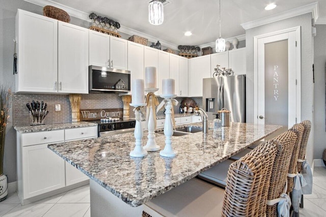 kitchen featuring white cabinetry, stainless steel appliances, an island with sink, decorative backsplash, and hanging light fixtures