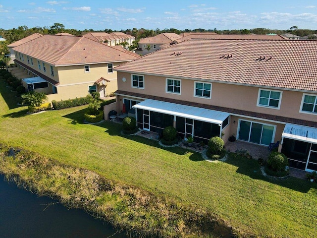 back of property featuring a lawn, a water view, and a sunroom