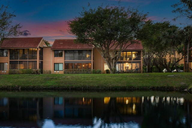 back house at dusk with a water view and a lawn