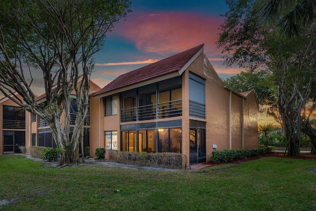 back house at dusk with a balcony and a yard