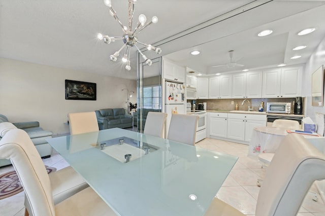 dining space with light tile patterned floors, ceiling fan with notable chandelier, a raised ceiling, and sink