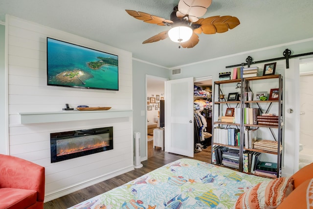 bedroom featuring ceiling fan, a large fireplace, dark wood-type flooring, ornamental molding, and a closet