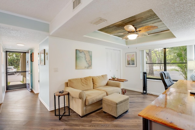 living room with dark wood-type flooring, ornamental molding, a tray ceiling, and ceiling fan