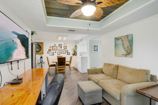 living room with a tray ceiling, ceiling fan, wood-type flooring, and a textured ceiling