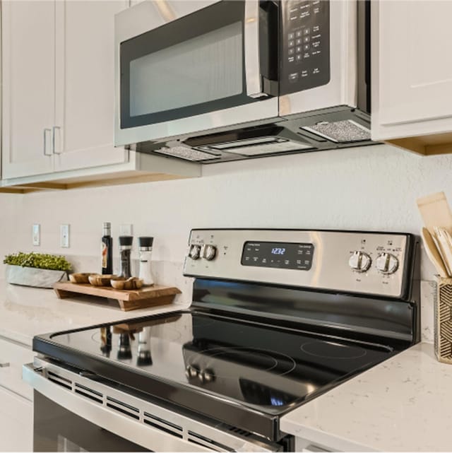 kitchen with appliances with stainless steel finishes, light stone counters, and white cabinetry