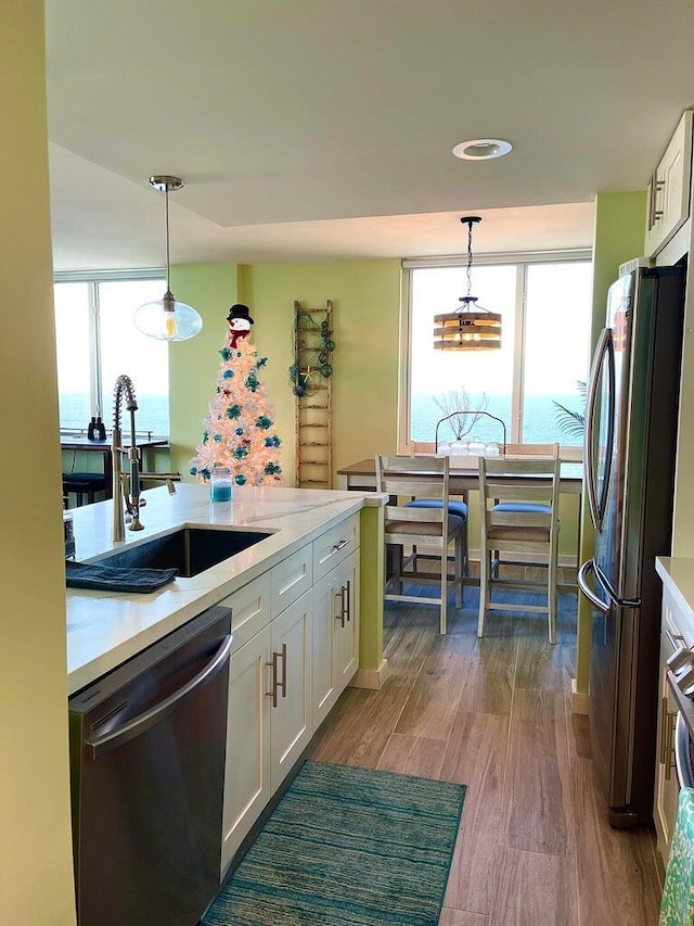 kitchen featuring stainless steel appliances, dark wood-type flooring, hanging light fixtures, white cabinets, and sink