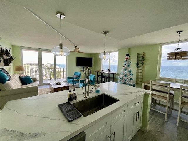 kitchen with a healthy amount of sunlight, hanging light fixtures, white cabinets, light stone counters, and sink