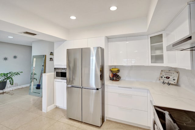 kitchen featuring tasteful backsplash, white cabinetry, stainless steel fridge, light stone counters, and wall chimney range hood