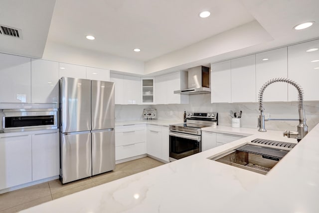 kitchen with tasteful backsplash, white cabinets, light tile patterned floors, stainless steel appliances, and wall chimney exhaust hood