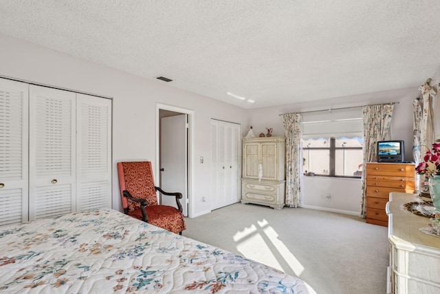 bedroom featuring multiple closets, a textured ceiling, and light carpet