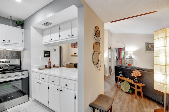 kitchen with stainless steel electric range, light hardwood / wood-style floors, and white cabinets