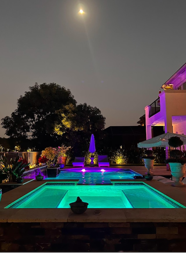 pool at dusk with an in ground hot tub