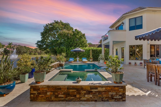 pool at dusk featuring a patio area and an in ground hot tub