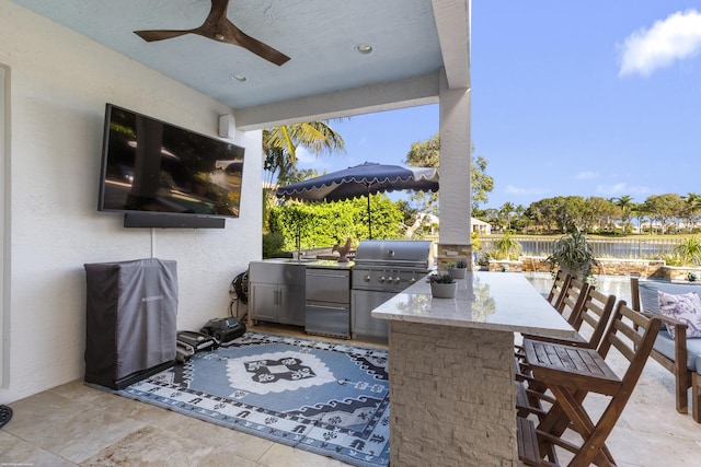 view of patio with exterior kitchen, grilling area, a bar, and ceiling fan