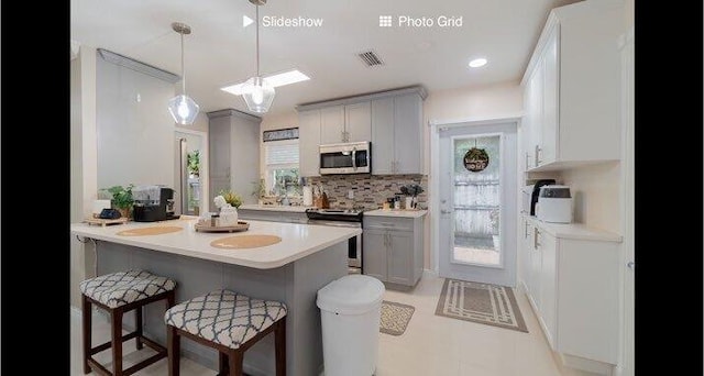 kitchen featuring a breakfast bar area, appliances with stainless steel finishes, decorative light fixtures, and gray cabinets