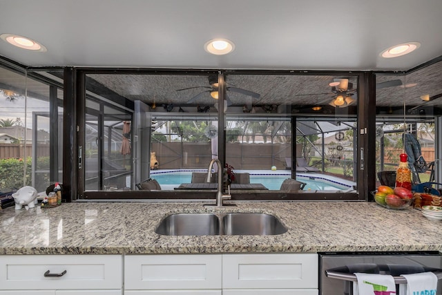 kitchen with dishwasher, white cabinetry, sink, ceiling fan, and light stone counters