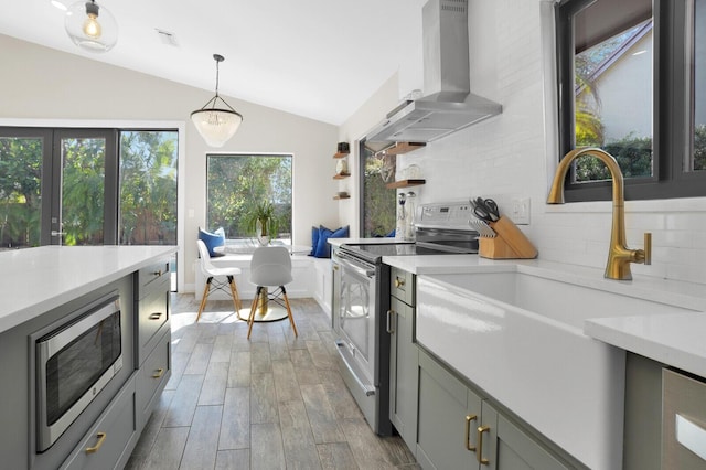 kitchen with pendant lighting, appliances with stainless steel finishes, lofted ceiling, wall chimney range hood, and gray cabinets