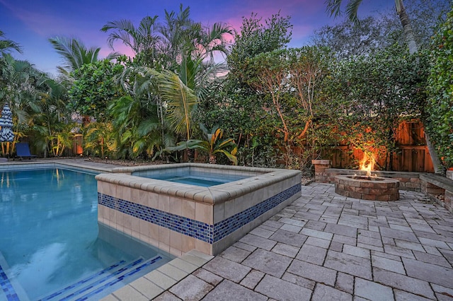 pool at dusk with an in ground hot tub, a fire pit, and a patio